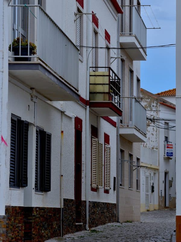 Row of ivory white houses in Nazaré with colourful louvred windows and matching balconies along a flat, easy to walk street