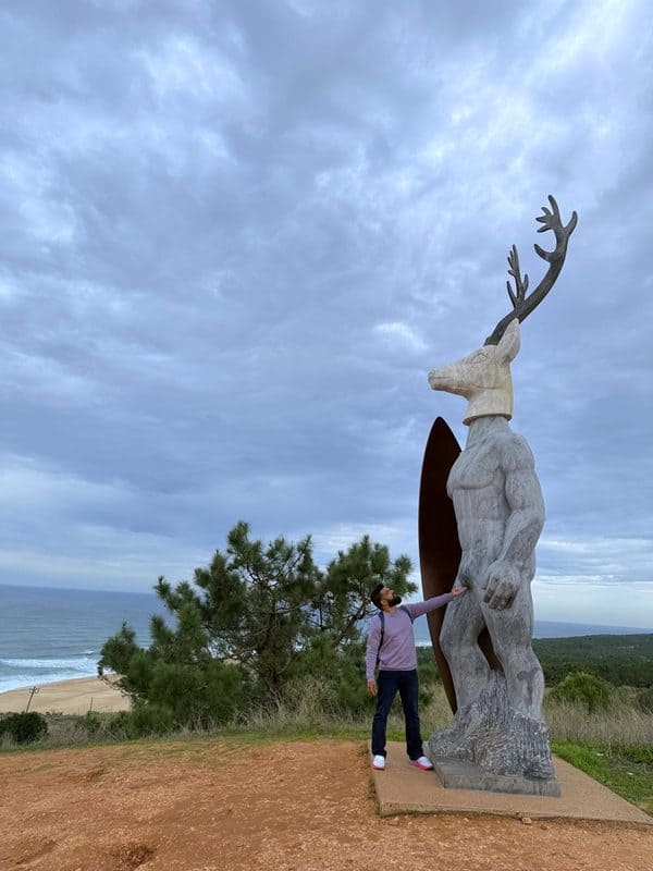 vacaywork author ashrith standing next to Veado statue with deer head and surfer body overlooking forest and north beach