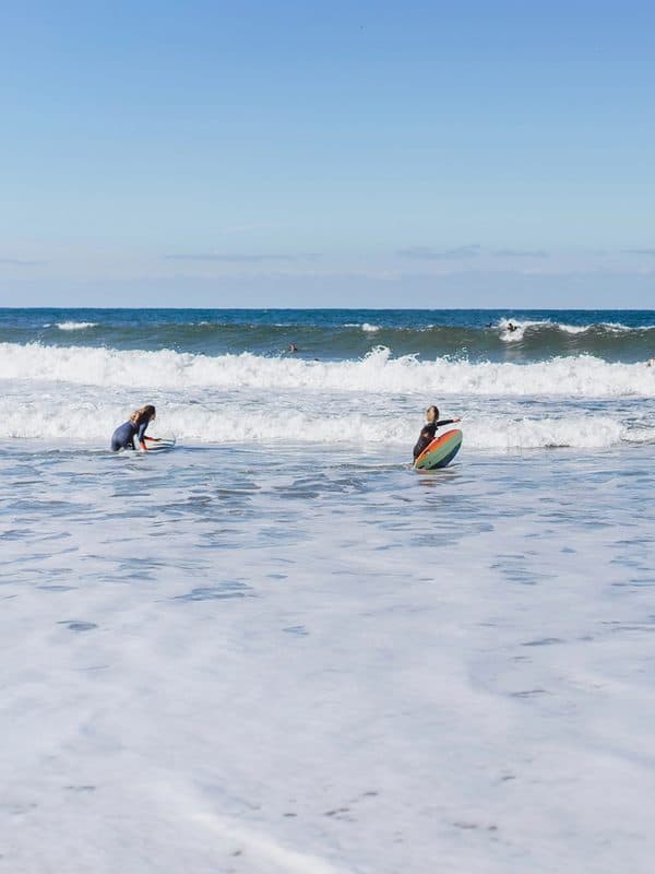 Two young teenagers learning to surf on boards at Praia do Norte Beach in Nazaré on a sunny day