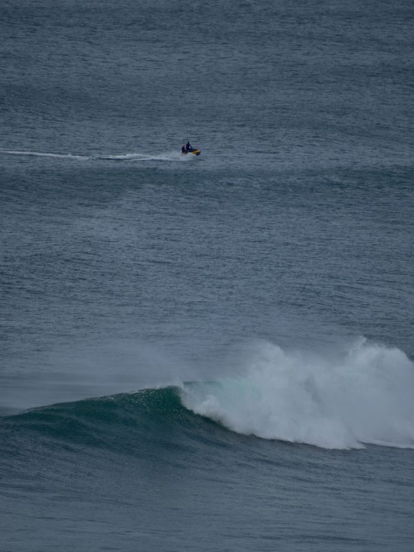 Tourist riding with a professional surfer through the waves at Praia do Norte in Nazaré