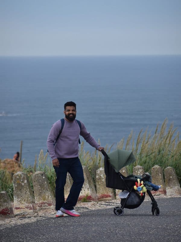 Vacaywork author Ashrith Shetty standing with his son in a stroller on the Lighthouse Road, with the Atlantic Ocean behind them
