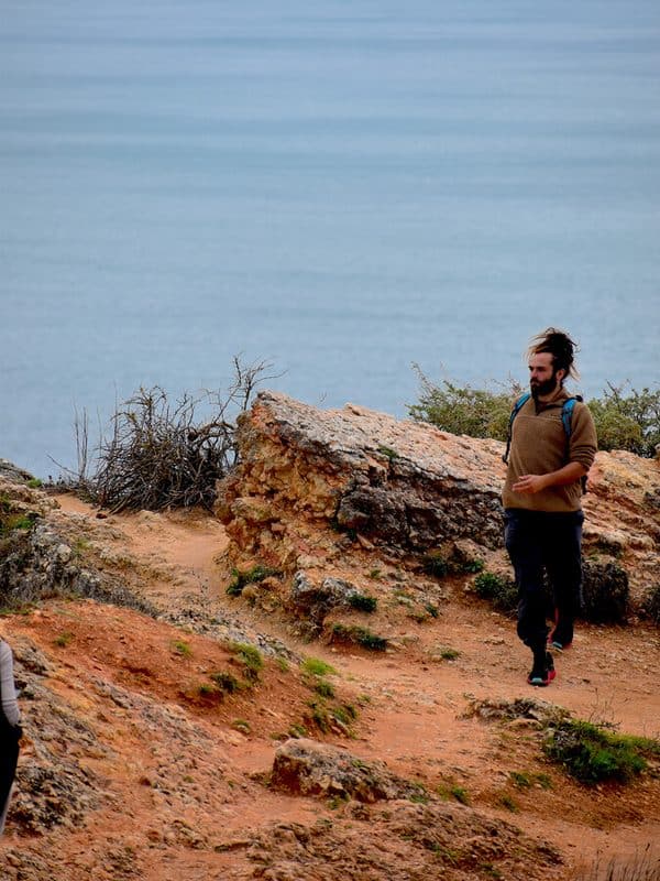 Nazare Portugal coastal trail with rocky ground, ocean views and a young hiker walking beside the cliffs
