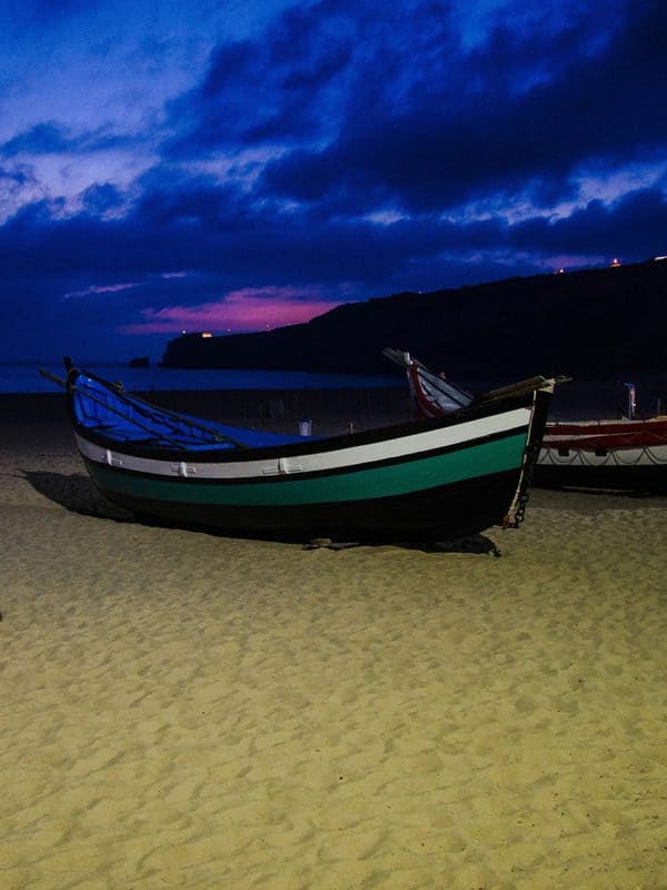Traditional Nazaré boats resting on the sandy shore at night, with a dark blue and pink sky after sunset