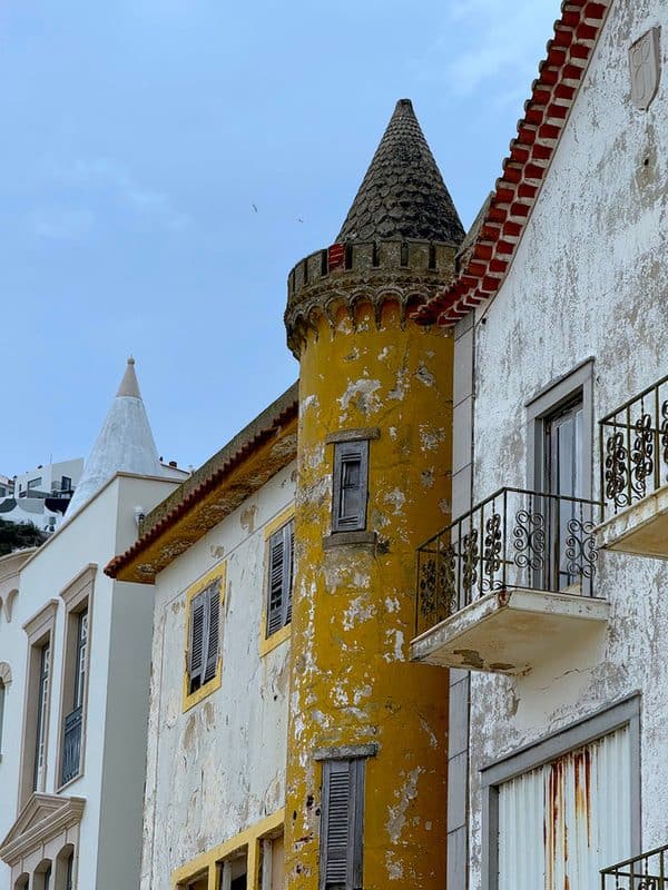Pastel houses in Nazaré with conical towers and worn cast iron balconies, showing the weathered character of the old town